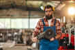 © Zamrznuti tonovi - Young bearded man in a workshop holding grinding machine in his hands.