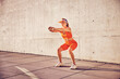 © baranq - Athletic adult woman doing squat exercise outdoors against concrete wall