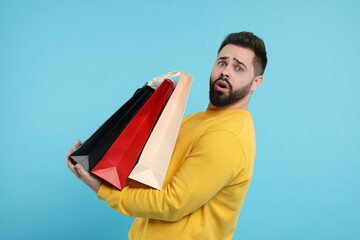 Sticker - Shocked man with paper shopping bags on light blue background