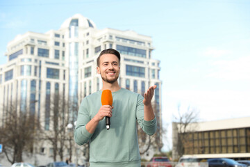 Wall Mural - Young male journalist with microphone working on city street