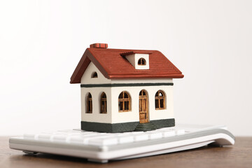 Wall Mural - Mortgage concept. House model and calculator on wooden table against white background, closeup