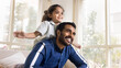 © fizkes - Cheerful young Indian father piggybacking sweet daughter kid, playing airplane flight, carrying child on back, looking away, smiling, laughing. Cute positive girl and dad enjoying leisure. Banner shot