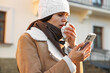 Woman with tissue blowing runny nose while using phone outdoors. Cold symptom