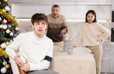 Poster - Domestic quarrel during Christmas celebration - father and sister scolding young guy in home kitchen