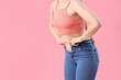 Young woman in tight jeans on pink background, closeup. Weight gain concept