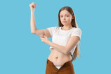 Fototapeta Panele - Young woman in tight pants with chubby arms on blue background. Weight gain concept