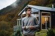 Young man in casual clothes Holding coffee mug near modern cottage between hills