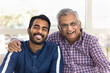 © fizkes - Cheerful elderly Indian father hugging young adult son, touching shoulder with support, parents pride, looking at camera with toothy smiles, laughing, having fun, posing for head shot portrait