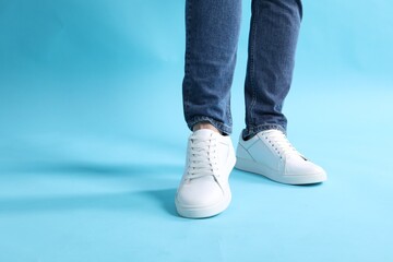 Poster - Man wearing stylish white sneakers on light blue background, closeup