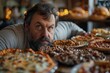 A man with a full beard and casual attire sits among an abundance of food giving a wary, overwhelmed look