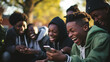 A group of young people gathers outdoors, immersed in their smart mobile phone devices, laughter and friendly banter filling the air as they play video games apps together .