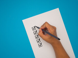 Hand-holding a pen, mark five correct sign symbols in boxes on white paper over a blue background.