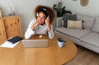 © Daniel - Young African American woman working at home office using wireless headphones. Happy Hispanic female using laptop.