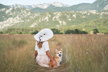 Wall Mural - Happy girl walk with dog. Pembroke Corgi with woman in Hat on nature on the field in summer