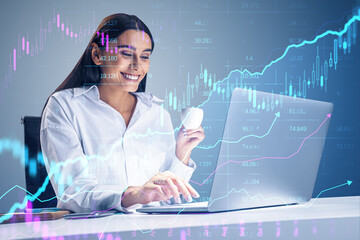 Wall Mural - Attractive happy businesswoman using laptop at desk with creative glowing candlestick forex chart on blurry background. Financial trade and market concept. Double exposure.