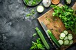 Fresh various vegetables, cut zucchini, wooden cutting board and knife on rustic dark background top view. Cooking vegetarian meal from healthy ingredients, diet food and nutrition concept