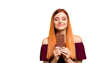 Sticker - Cute red-haired young woman with pleasure and dreaminess holds a chocolate in her hands isolated on yellow background with copy space for text