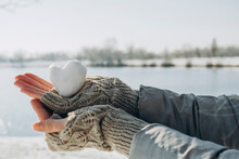 Hands Of Woman Holding Heart Shaped Snowball Near Lake