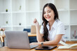 © SOMKID - Happy young asian woman wearing earphones and using laptop computer at desk in office, Female asian student with laptop computer, College female student learning online.