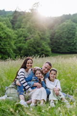 Wall Mural - Beautfiul young family sitting in grass at meadow, enjoying together time.