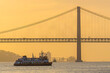 Tagus river with suspension bridge and boat at sunset in Lisbon, Portugal