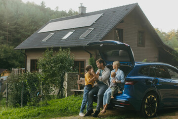 Family with electric car standing in front their house with solar panels on roof. Solar energy and sustainable lifestyle of young family. Concept of green energy and sustainable future for next