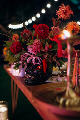 Wall Mural - Variegated multi-colored flower arrangements in vases in the shape of a skull, Mexican style in the decor. On the festive table in the wedding banquet area, compositions of flowers and greenery, candl