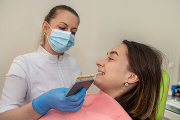 Orthodontist choosing the shade with tooth color chart near of face woman client