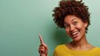 dark skinned female with Afro haircut, points away with both fore fingers, shows blank space for your promotion, isolated over mint green background. People, advertisement concept