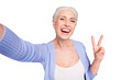 Self portrait of grey haired old nice beautiful cheerful smiling woman showing v-sign gesture. Isolated over violet purple background