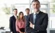 © opolja - Smiling confident mature businessman leader looking at camera standing in office at team.