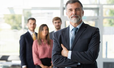 Wall Mural - Smiling confident mature businessman leader looking at camera standing in office at team.