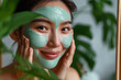 Woman applying facial clay mask. Beautiful asian girl with green cosmetic peel off mask on her face. Natural skin care and cleansing concept, beauty and spa treatment