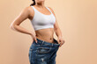 © Prostock-studio - Fit woman confidently demonstrating successful weight loss by pulling out oversized jeans,