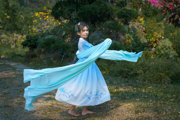 Pretty Asian girl in a beautiful elegant ancient Chinese costume traditional dress dancing with a flowing shawl made of thin long fabric pastel color waving in the wind at a green natural garden. 