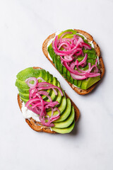 Wall Mural - Avocado toast with cream cheese and pickled red onions on white plate.