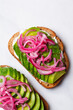 Avocado toast with cream cheese and pickled red onions on white plate.