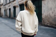 Back view of a fashionable blonde woman in a blank white sweatshirt on the street. Mock-up for design. Blank template