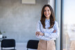 © Dragana Gordic - Successful businesswoman standing in creative office and looking at camera. Young woman entrepreneur in a coworking space smiling. Por of business team at modern agency with copy space.