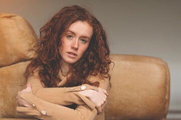 Wall Mural - portrait of a young redhead woman in a brown shirt sitting on the floor near a couch at home