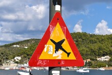 Bright Warning Sign Next To Skiathos Airport Runway, Greece, Informing Pedestrians Of Low Flying Overhead Airplanes. 