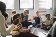 © Maskot - Senior female teacher playing with group of preschool children while sitting in classroom at kindergarten