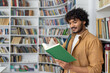 © Liubomir - An adult male stands in a well-lit library, immersed in reading a green book. Bookshelves filled with various books surround him, suggesting a quiet atmosphere for study and literature exploration.