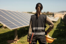 Rear view of female engineer standing with hand on hip while looking at solar panels in field