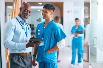 Wall Mural - Male Doctor And Nurse In Scrubs With Digital Tablet Meeting In Hospital With Colleagues Behind