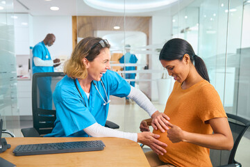 Wall Mural - Female Nurse Or Doctor Wearing Scrubs Examining Pregnant Woman In Hospital Obstetrics Clinic