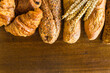 Frame of various french breads (baguette, croissants, chocolate pies) and bunch of wheat's ears on a wooden background; copy space
