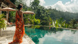 A woman wearing a sarong stands at the edge of an infinity pool, gazing out over a lush forest