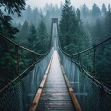 Fototapeta Mosty linowy / wiszący - Misty suspension bridge in forest - A majestic suspension bridge spans across a lush forest shrouded in fog, adding mystery to the tranquil scenery
