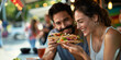 Happy couple sharing tacos in front of a Mexican Food Truck sitting by outdoor dining table have a lot of fun, sweet heart warming romantic scene of lovers dating backgrounds with copy space.
